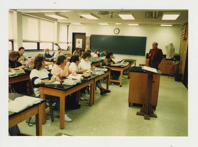 A male professor teaches while students listen