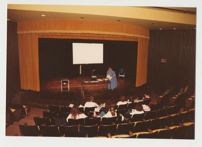 A female professor addresses a class meeting in a theater