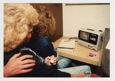 Female students look at an audio visual machine which has visual and a cassette audio tape for class use in the library