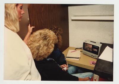 Female students look at an audio visual machine which has visual and a cassette audio tape for class use in the library