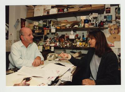 Professor Robert McAninch sits at the desk in his office while speaking with an unidentified woman