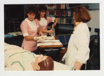 Female students work with a mannequin while an unidentified female professor (right) watches