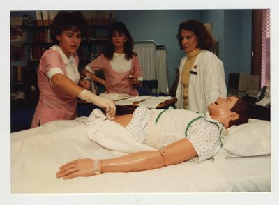 Female students work with a mannequin while an unidentified female professor (right) watches