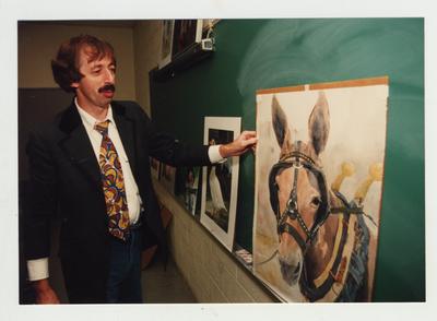 A male professor examines paintings in a classroom