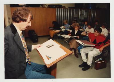 A male professor lectures in front of a classroom as students listen