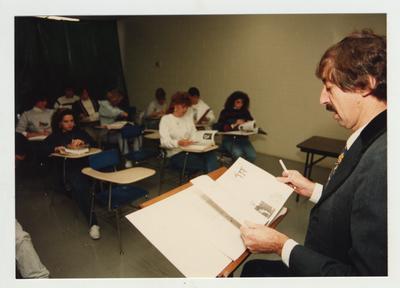 A male professor lectures in front of a classroom as students listen