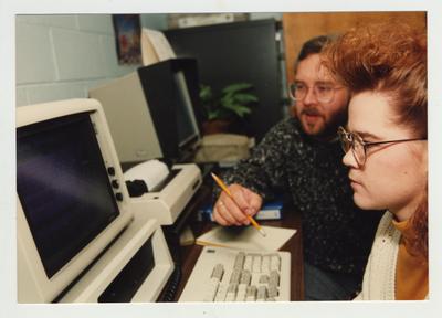 A man helps a female student on a computer