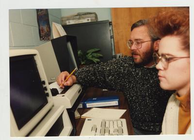 A man helps a female student on a computer