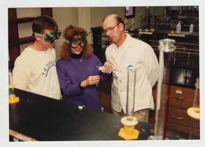 A male Chemistry professor watches students perform an experiment