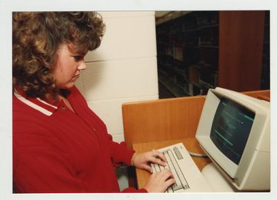 A female student uses a computer in the library to locate books