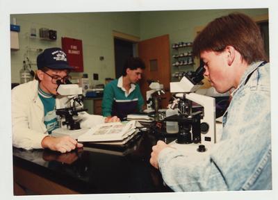 Male students look through microscopes in a laboratory classroom