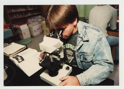 A male student looks through a microscope in a laboratory classroom