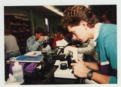 A male student looks through a microscope in a laboratory classroom