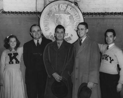Photo of Adolph Rupp and others during a celebration of the SEC championship team, held in Alumni Gym, March 06, 1940; pictured left to right are Marcia Willing, cheerleader, Rupp, Lexington Mayor T. Ward Havely, Layton Rouse, team captain, and Bill Elder, head of SUKY, a UK student organization; photo received June 13, 1959 from the Cincinnati Enquirer