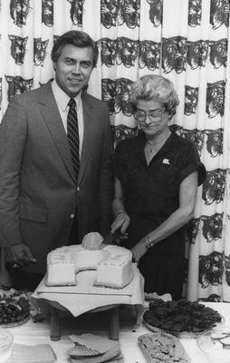 Jane S. Rollins, administrative assistant to basketball coach Joe B. Hall, cutting a cake; athletics director Cliff Hagan is to her right