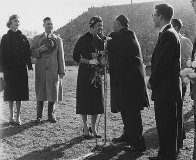 Mrs. Frank Dickey (far left), UK President Frank Dickey (2nd from left) and other unidentified people are watching UK Trustee and former Governor A. B. Chandler kiss the unidentified Homecoming Queen at Stoll Field; photographer:  University of Kentucky