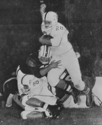 UK football player Bobby Cravens (28) is tackled by Auburn player Jimmie Ricketts as Cravens tries to get over his own teammate Jim Miller (60) during an October 12, 1958 game. Received December 1, 1958 from Public Relations
