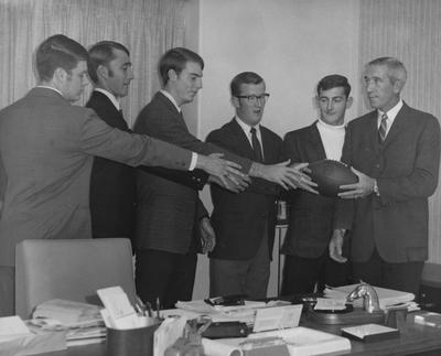 Six unidentified UK football players posing with a football; Coach Charlie Bradshaw is at far left