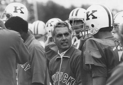 UK Head football coach Fran Curci (1973-81) talks with several unidentified players in uniform during game