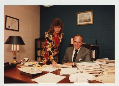 A woman shows a document to a man sitting at a desk