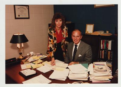 A woman shows a document to a man sitting at a desk