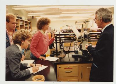 A male professor and his students look at a machine in a laboratory