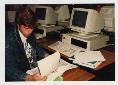 A male student types on computers in a classroom