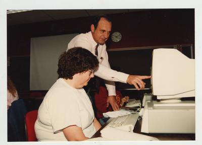 A male professor helps a female student in a computer class