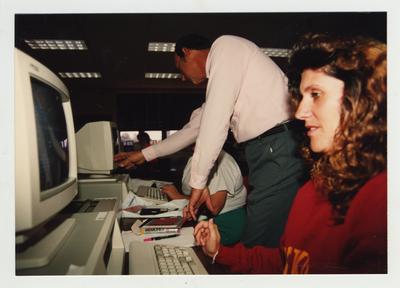 A male professor helps two female students in a computer class