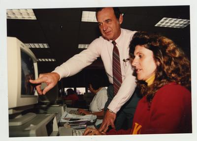A male professor helps a female student in a computer class