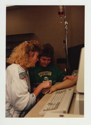 Female students practice putting an I. V. into the hand of a mannequin