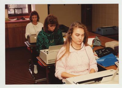 Female students type on typewriters in a classroom