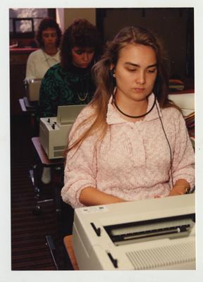 Female students type on typewriters in a classroom
