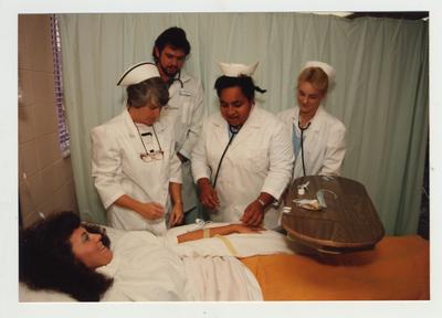 A female African - American nursing student practices on another female student as others look on