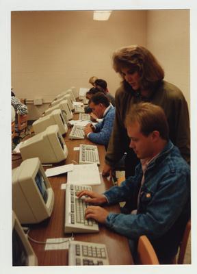 A female student helps a male student with a computer in a classroom