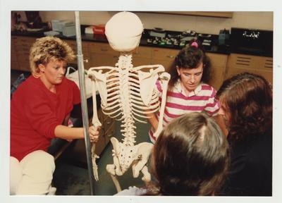 Female students look at a skeleton in a classroom