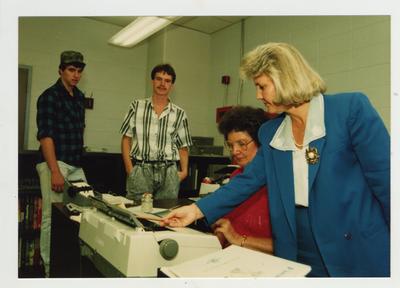A woman helps a female student with a typewriter while male students look on