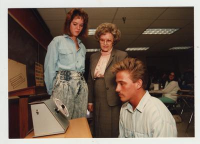 A female professor and student look on as a male student examines an object