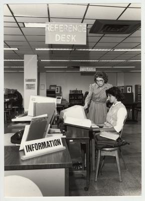 Norma Jean Gibson (woman standing with glasses), reference librarian, helps a female student in the Reference Area on the first floor of the Margaret I. King Library; This image was submitted for use in the 1983 / 1984 O. C. L. C. Annual Report