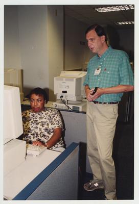 Mark Ingram helps Shirley Greene, who is working at a computer in the Medical Library (located in the Medical Center); Photographer: Mark Minor