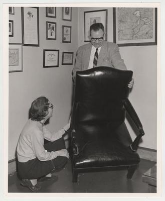 The vice - president's chair, which was presented to Alben W. Barkley by the Kentucky Democratic members of the House in 1949 as a token of affection and in recognition of long and outstanding service to Kentucky, to the nation and humanity, is now located at the University of Kentucky; During a preliminary inspection of the various articles deposited by the Barkley family, Dr. Jacqueline Page Bull, head of the UK Library's Archives Department, and Dr. Bennett H. Wall, University History professor, pause momentarily to admire the chair
