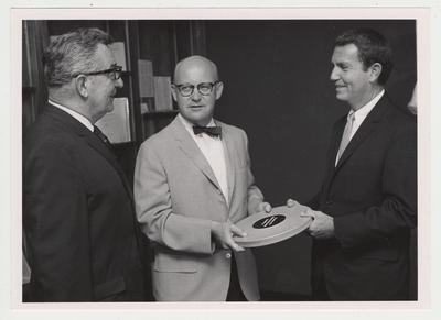 Dr. Stuart Forth (center), director of University of Kentucky Libraries and acting vice - president of student affairs, accepts a film of the retirement ceremony of Senator Thurston B. Morton, Louisville, from Lee Browning (right), station manager of WAVE - TV, Louisville, while Bill Gladden (left), station promotion manager, looks on; WAVE made the film especially for the UK Library's Special Collections