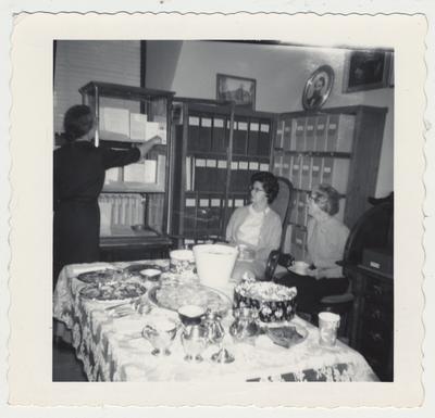 Open house for Library staff; From left: Mary Hester Cooper, Genevieve S. Johnston, and Margaret Tuttle; Cooper is arranging material in the exhibit case; Johnston sits in Dr. Patterson's chair and his desk is in the corner of the picture
