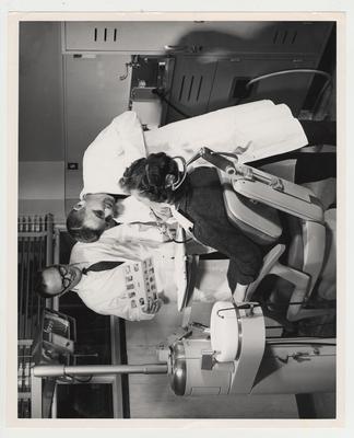 Roy T. Durochen, associate Professor of Oral Medicine (center), works on Mrs. Pat Russell, secretary of Dentistry (seated), while Harry M. Bohannan, Associate Professor of Perodontics and Endodontics (left) watches