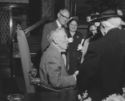 James W. Carnahan (seated, left) shaking hands with people at reception for Carnahan House dedication
