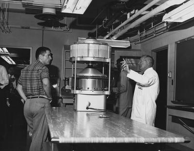 Six unidentified men looking at a machine in a laboratory