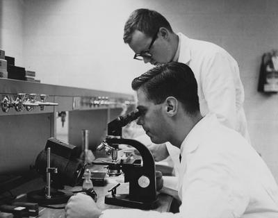 Two unidentified men are working in a laboratory. One man is looking through a microscope