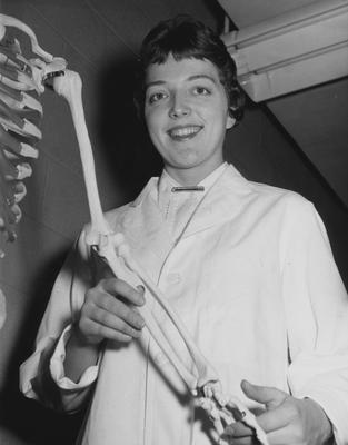 An unidentified woman is holding the arm bone of a class skeleton model