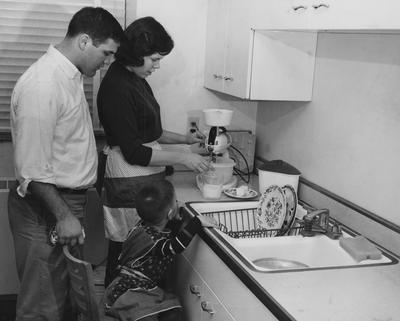 Mr. and Mrs. Duke Curnette, and son, using a mixer in the kitchen of the new Cooperstown Apartments. Received on March 22, 1957 from Public Relations