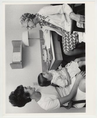 A female medical center employee speaks with a mother and her daughter in an office